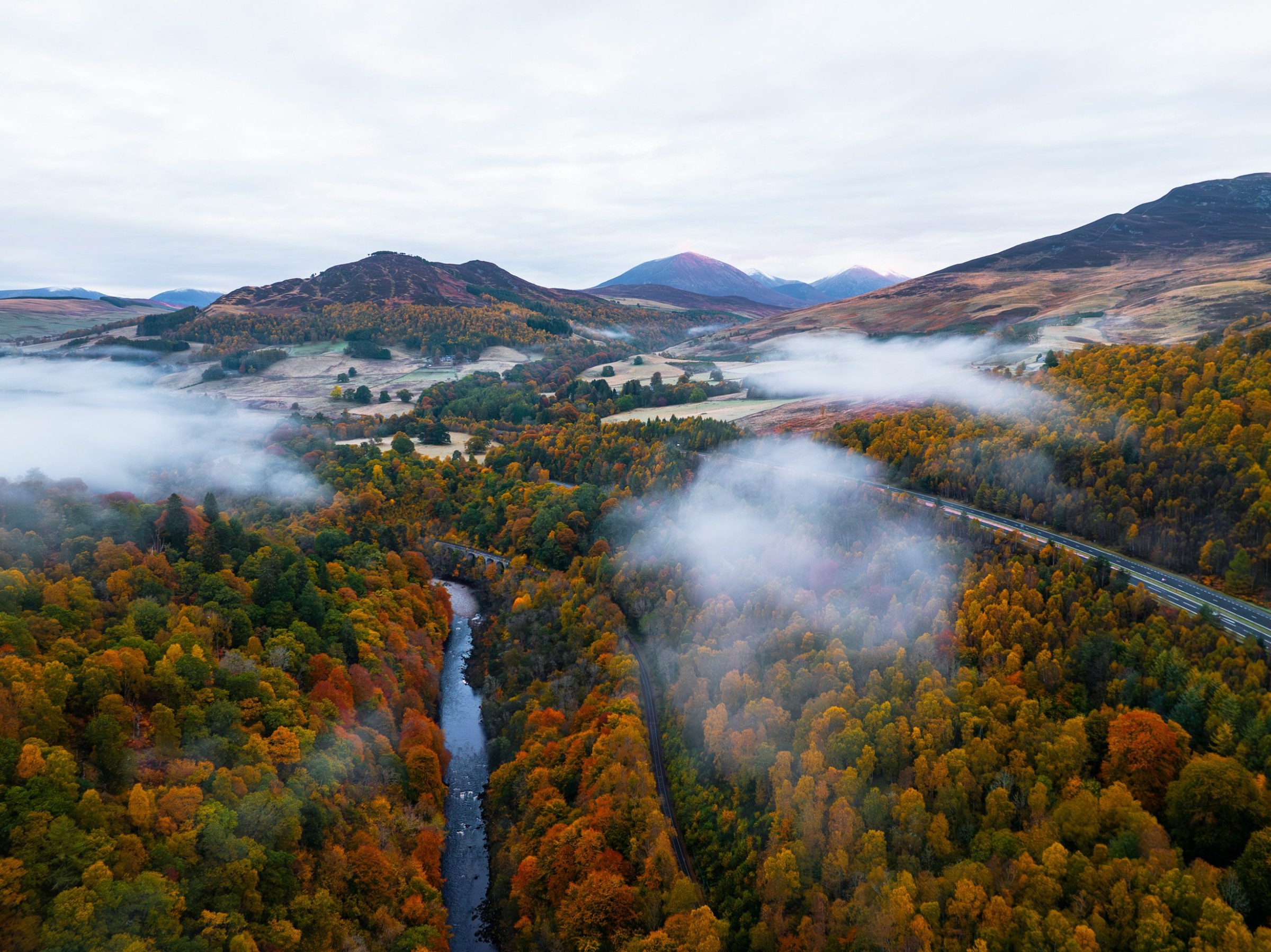Aerial of a river, road and misty valley in peak fall color with mountains beyond