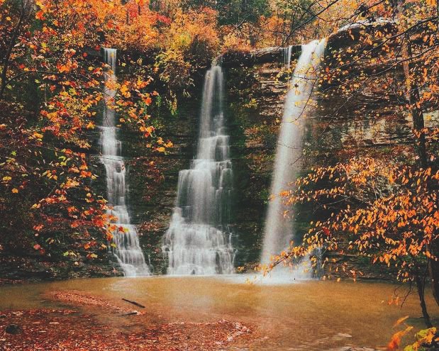 Three waterfalls dropping over a rock ledge into a pool, framed by trees in orange fall color