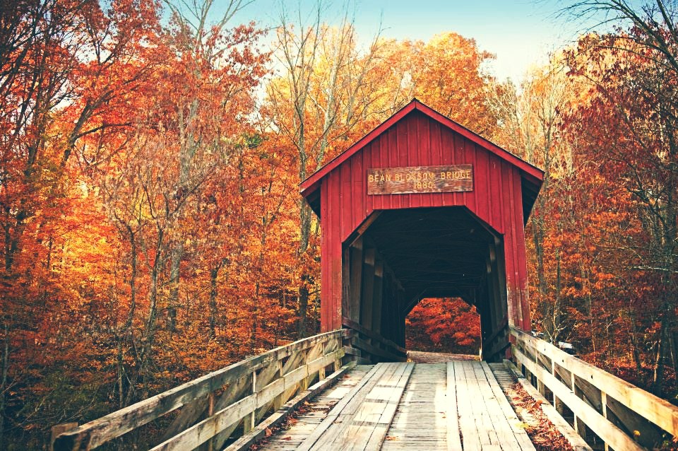 A red covered bridge on a wooden approach, surrounded by trees in orange fall color